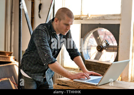 Side view of male carpenter using laptop in workshop Stock Photo