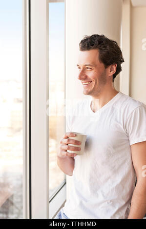 Smiling man drinking coffee and looking though window Stock Photo