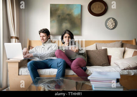 Young couple using technologies on sofa at home Stock Photo