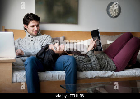 Cheerful young couple using technologies while relaxing on sofa Stock Photo
