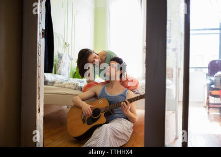 Man playing guitar while looking at girlfriend in bedroom Stock Photo