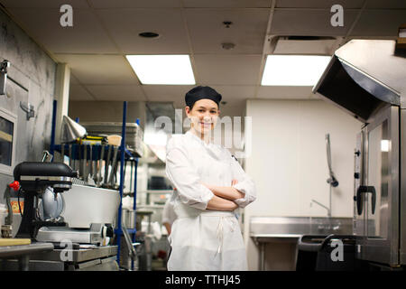 Portrait of happy chef with arms crossed standing in commercial kitchen Stock Photo