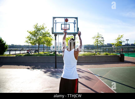 Rear view of sportsman throwing basketball in hoop on sunny day Stock Photo