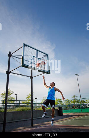 Man dunking ball in hoop at park against sky Stock Photo