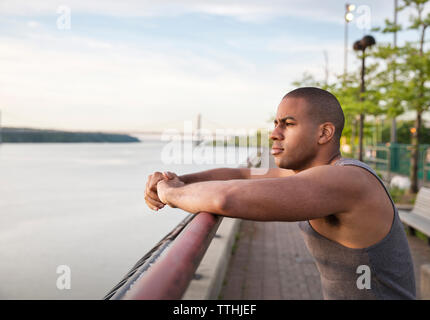 Thoughtful man standing at railing in park by river against sky Stock Photo