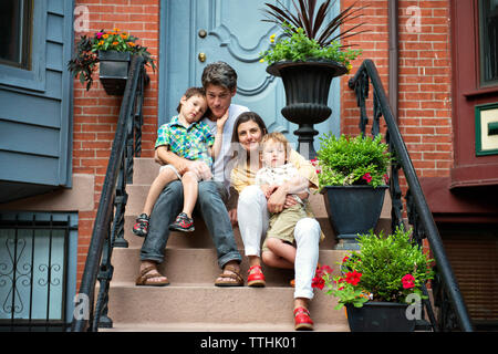 Portrait of smiling family sitting on steps outside house Stock Photo