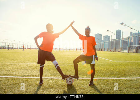 Portrait of happy sportswomen giving high-five with soccer ball on field during sunny day Stock Photo