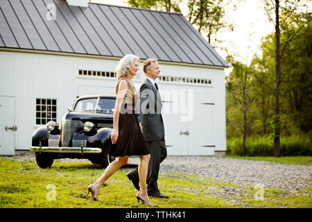 Senior couple walking on field against vintage car outside house Stock Photo