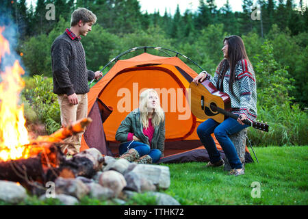 Happy woman playing guitar with friends at camping in forest Stock Photo