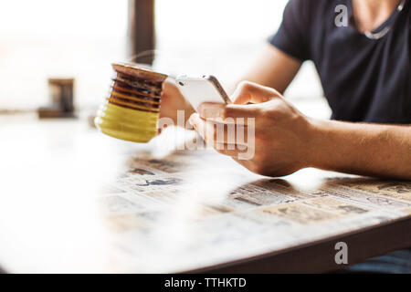 Cropped image of man using smart phone while drinking coffee on table Stock Photo