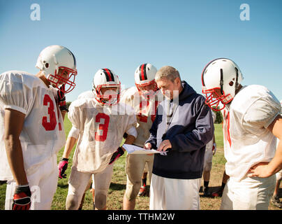 Coach explaining to American football players standing on field Stock Photo