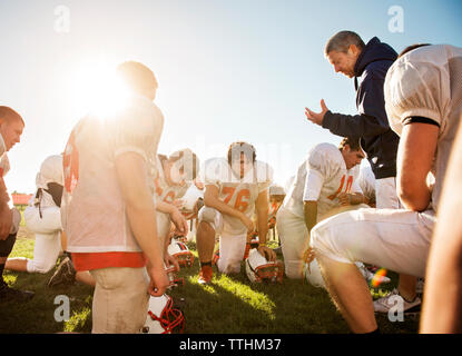 Confident coach giving training to players on American football field on sunny day Stock Photo