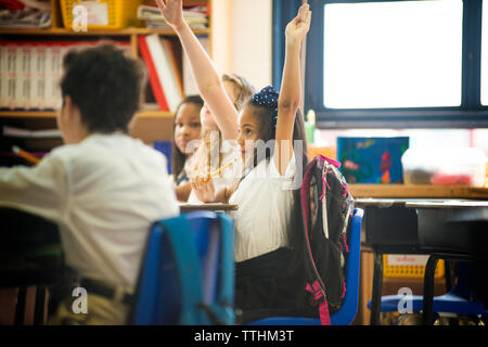Schoolgirls raising hands while sitting in classroom Stock Photo