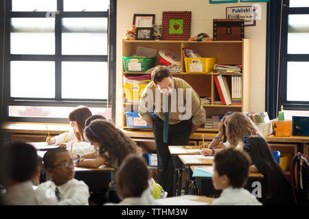 Teacher looking to children sitting at desks in classroom Stock Photo