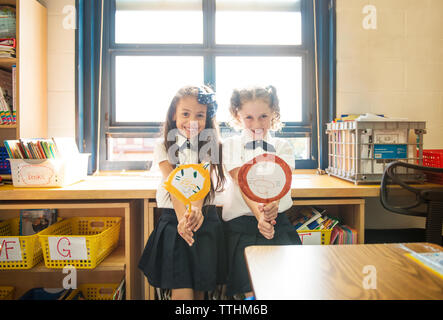 Portrait of happy schoolgirls holding craft products while standing in classroom Stock Photo