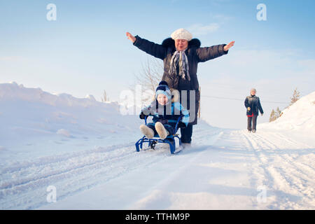 Cheerful woman pushing boy sitting on sled during winter Stock Photo