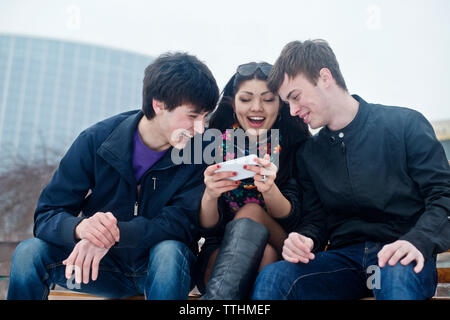 Happy friends using phone in park Stock Photo