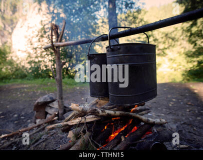 Containers heating over campfire at field Stock Photo