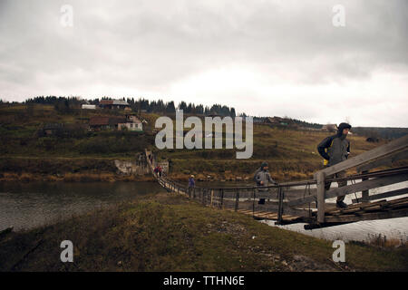 Hikers walking on footbridge over lake against cloudy sky Stock Photo
