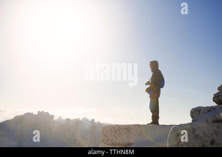 Side view of man standing on cliff against sky on sunny day Stock Photo