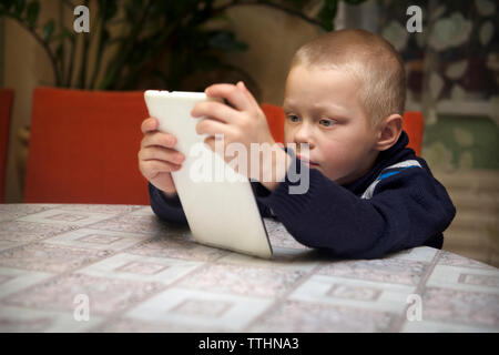 Boy using tablet computer while sitting at table Stock Photo