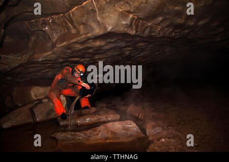 Manual worker removing water from boot while sitting in cave Stock Photo