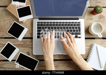 Female hands, laptop and photos on wooden background Stock Photo