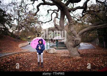 Girl holding umbrella while standing at park during autumn Stock Photo