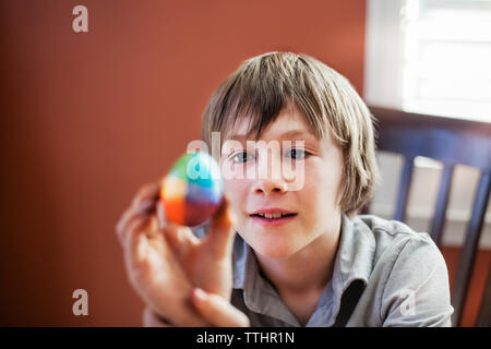 Boy looking at decorated easter egg while sitting on chair at home Stock Photo