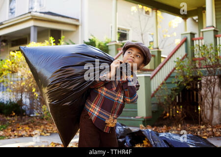 Boy looking away while carrying garbage bag at yard Stock Photo