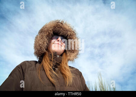 Low angle view of woman wearing fur hood against cloudy sky Stock Photo