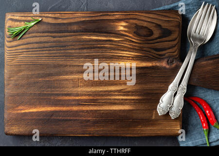 Cooking concept. Vintage cutting board with spices and cutlery on dark stone background. Copy space. Stock Photo