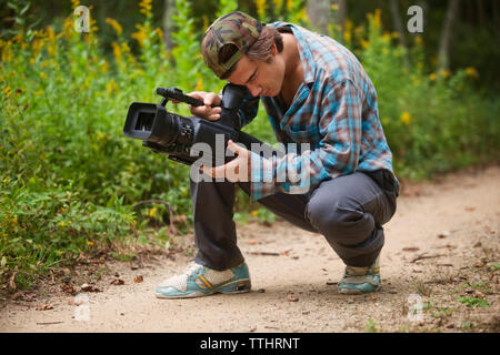 Man using video camera while crouching on dirt road Stock Photo