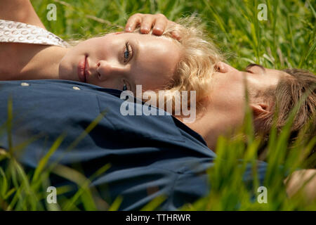 Portrait of woman leaning on man's chest while lying in grass field Stock Photo