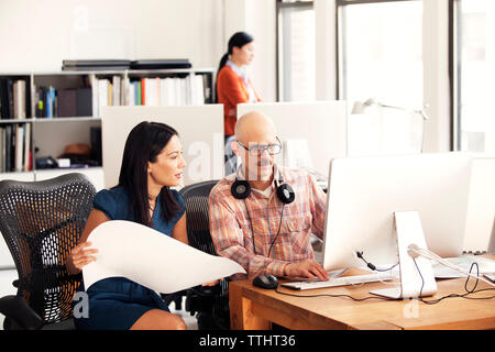 businessman and businesswoman discussing while sitting on chairs in office Stock Photo