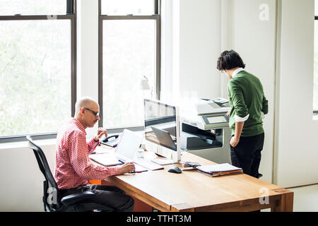 businessman working on computer while coworker using printer at office Stock Photo