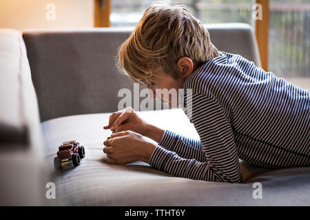 Boy playing with toys while lying on sofa at home Stock Photo