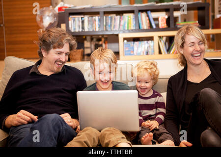 Siblings using laptop while sitting with parents on sofa at home Stock Photo