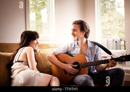 Man playing guitar while sitting with girlfriend on sofa at home Stock Photo