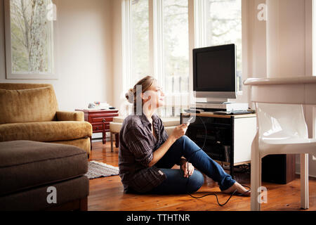Woman looking away while holding mobile phone at home Stock Photo