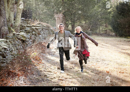 Happy couple running on field in forest during winter Stock Photo