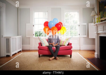Man holding helium balloons while sitting on sofa at home Stock Photo