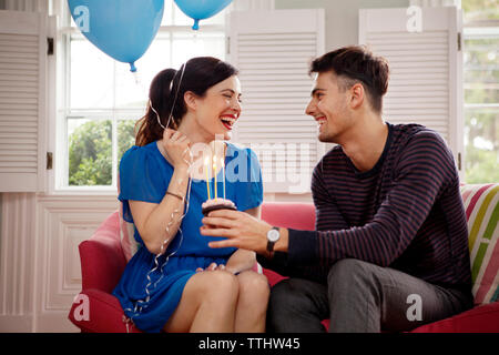 Happy couple celebrating birthday while sitting on sofa at home Stock Photo