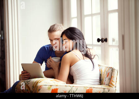 Happy couple using tablet computer while sitting on armchair at home Stock Photo