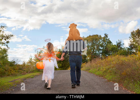 Rear view of father with children in Halloween costume walking on field Stock Photo