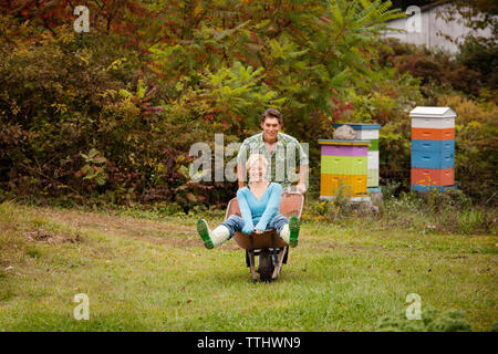 Man pushing woman in wheelbarrow on grass field Stock Photo