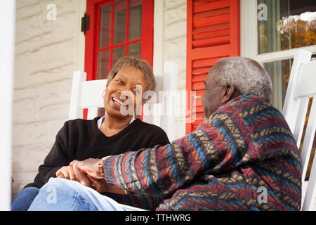 Senior couple holding hands while sitting against house Stock Photo