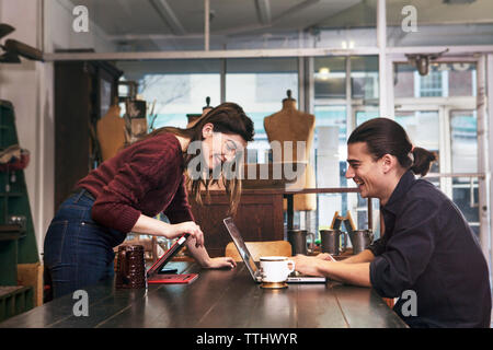Happy couple looking at laptop computer while sitting at clothing store Stock Photo