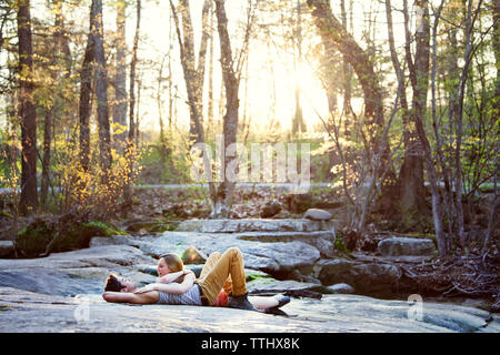 Happy couple talking while lying on rock at forest Stock Photo