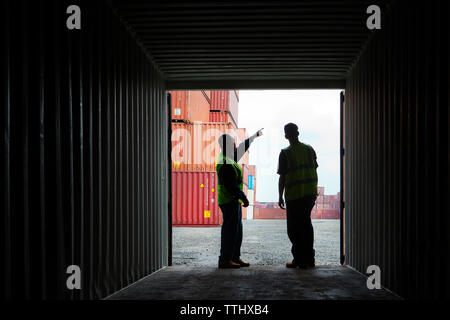 Worker pointing away while standing with man by cargo container at commercial dock Stock Photo